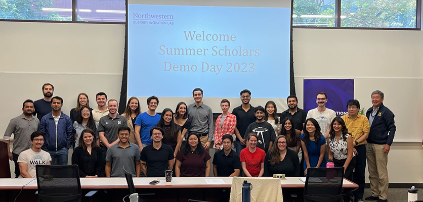 A group of people standing in front of a large screen that says demo day 2023